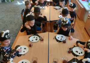 Dzieci siedzą przy stolikach degustują czarne potrawy.